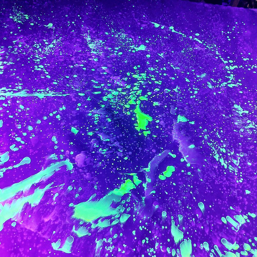 black latex sheet with a neon active splatter pattern under uv light